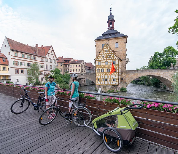 Radler auf dem Geyerswörthsteg blicken auf die Regnitz und das berühmte, mitten im Fluss stehende alte Rathaus in Bamberg. Foto: Markus Hammrich/Frankentourismus