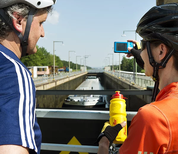 Zwei Radfahrer fotografieren ein Schiff, das gerade in der Schleuse Strullendorf geschleust wird.