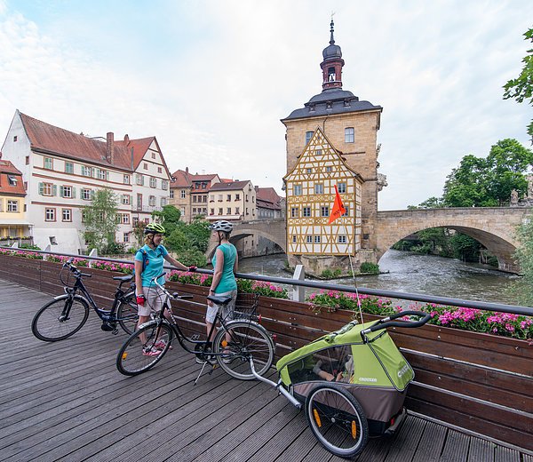 Radler auf dem Geyerswörthsteg blicken auf die Regnitz und das berühmte, mitten im Fluss stehende alte Rathaus in Bamberg. Foto: Markus Hammrich/Frankentourismus